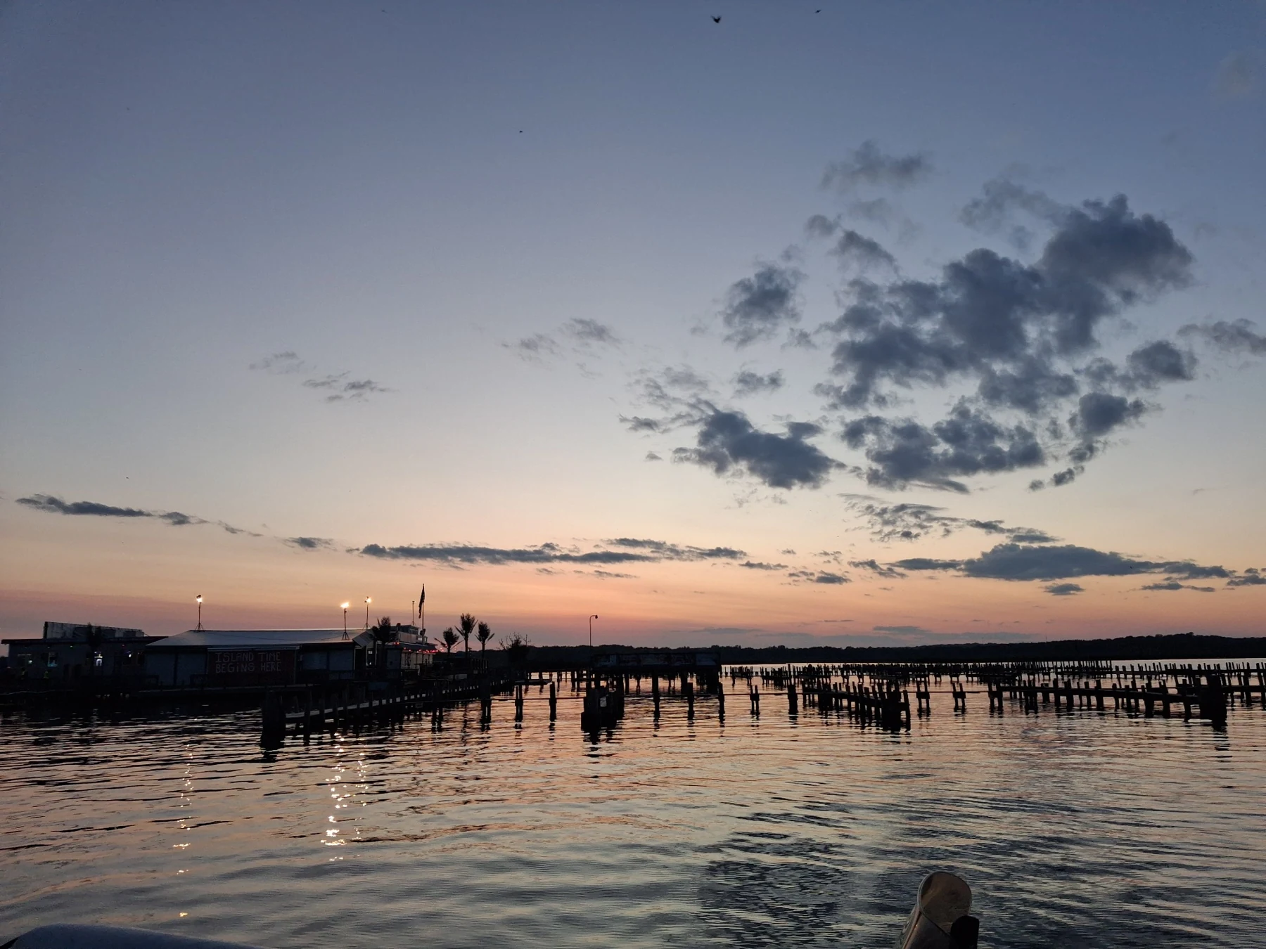 A waterfront pier and boats silhouetted against a pale peach and blue evening sky.
